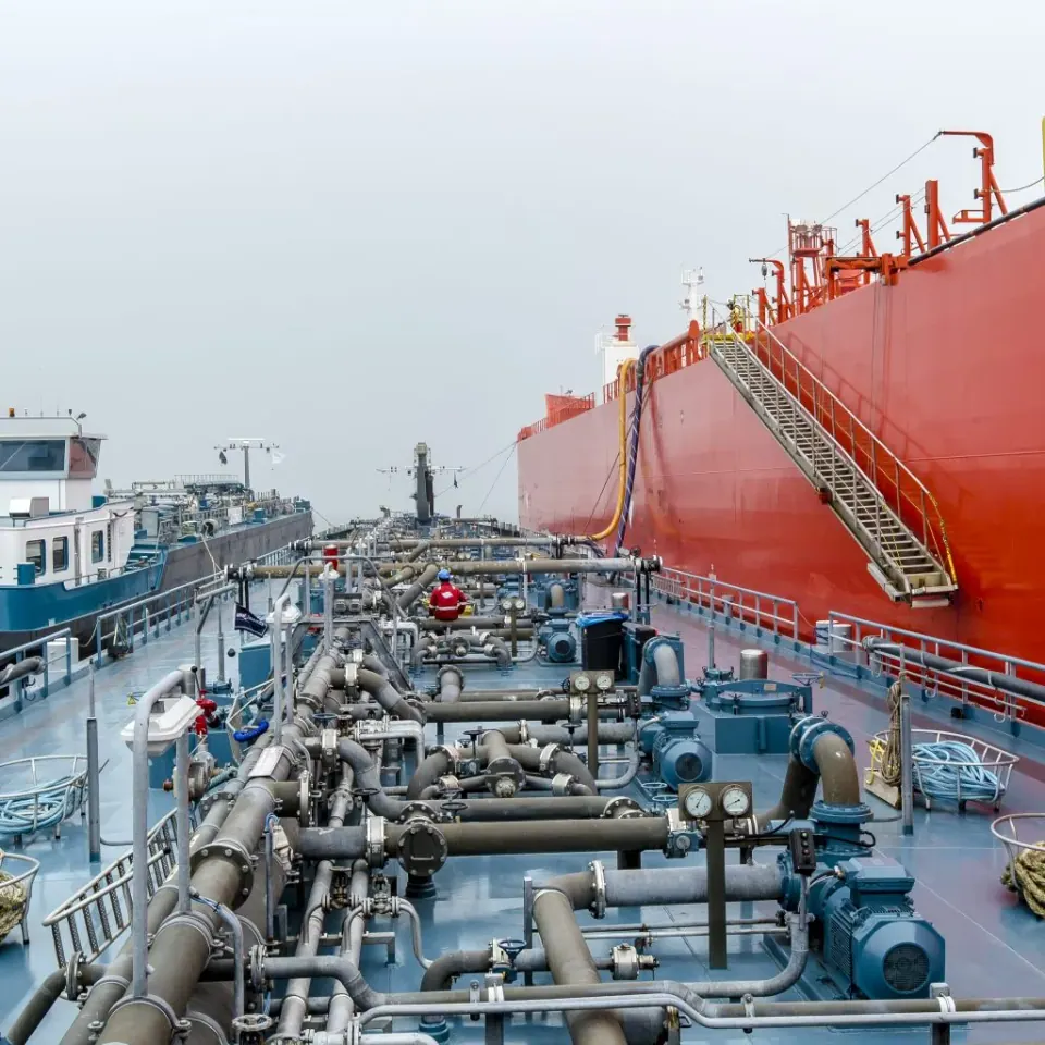 Het dek van een tanker met leidingwerk, langszij een groot zeeschip